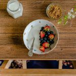 Aerial view of breakfast setup with a bowl of fresh fruits, milk, and granola on a wooden table.
