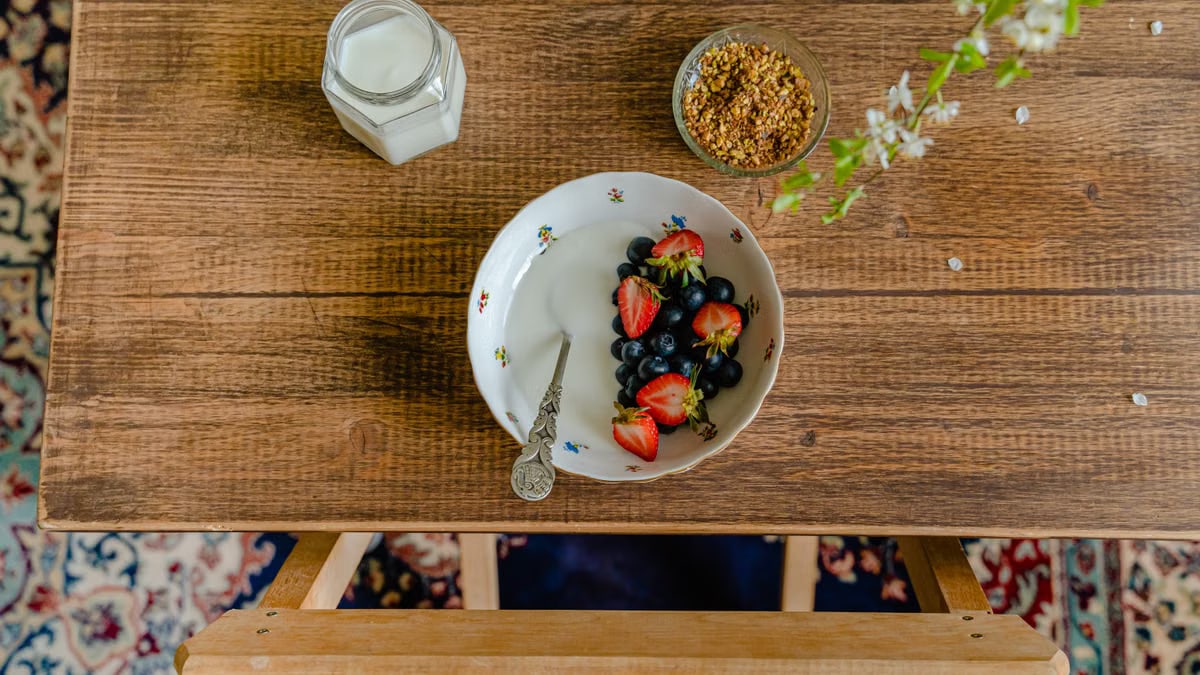 Aerial view of breakfast setup with a bowl of fresh fruits, milk, and granola on a wooden table.